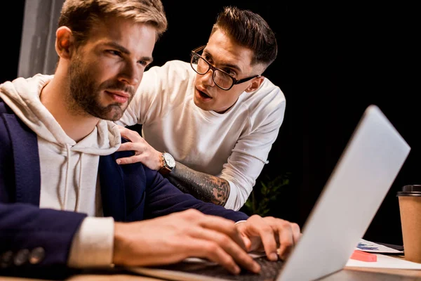 Молодий бізнесмен торкається плеча колеги, що працюють на ноутбуці вночі в офісі — стокове фото