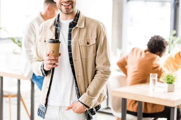 Частичный взгляд молодого бизнесмена, стоящего с рукой и карманом и держащего кофе, чтобы пойти — стоковое фото
