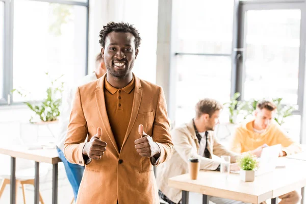 Alegre afroamericano hombre de negocios mostrando pulgares hacia arriba y sonriendo a la cámara - foto de stock