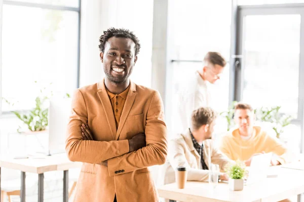 Cheerful african american businessman standing with crossed arms and smiling at camera — Stock Photo