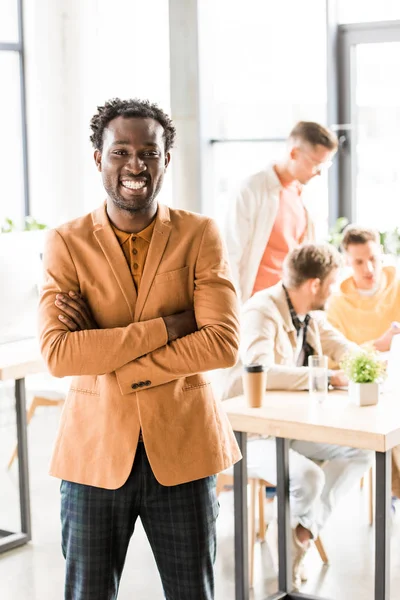 Feliz empresário afro-americano de pé com braços cruzados e sorrindo para a câmera — Fotografia de Stock