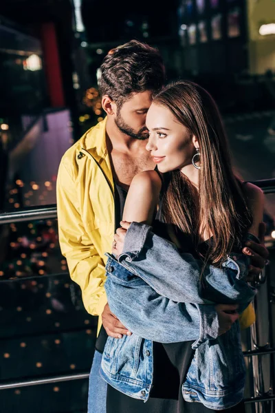 Guapo novio y atractivo novia en chaqueta abrazos en la noche de la ciudad - foto de stock