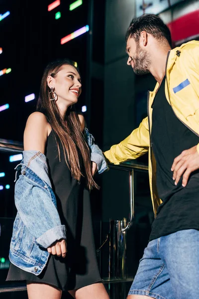 Atractiva novia y guapo novio sonriendo y hablando en la noche de la ciudad - foto de stock