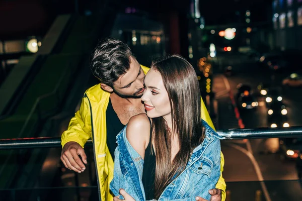 Alto ângulo vista de namorado beijando atraente e sorridente namorada na cidade da noite — Fotografia de Stock