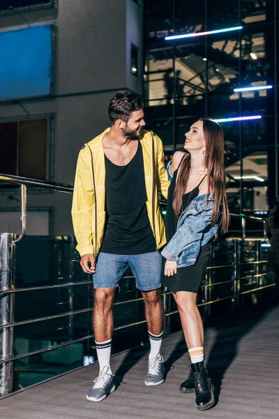 Atractiva novia y guapo novio abrazando y sonriendo en la noche de la ciudad - foto de stock