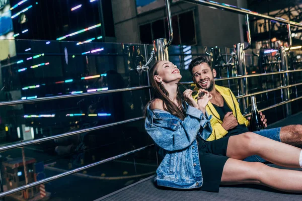 Schöner Freund mit Flasche und attraktive Freundin lächelnd in der Nacht Stadt sitzen — Stockfoto