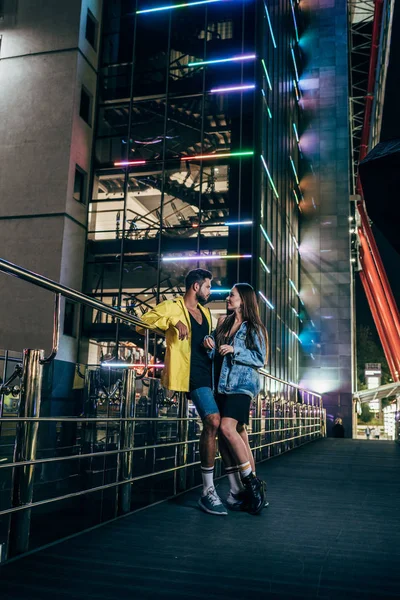 Vista lateral de novio guapo y novia atractiva sonriendo y hablando en la ciudad de la noche - foto de stock