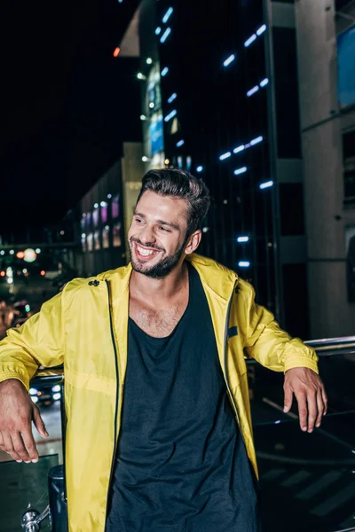 Handsome man in yellow jacket smiling and looking away in night city — Stock Photo