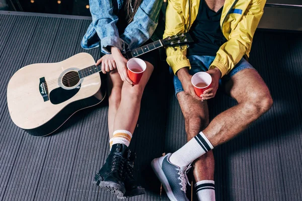 Vista recortada de novio y novia sosteniendo copas de plástico en la ciudad de la noche - foto de stock