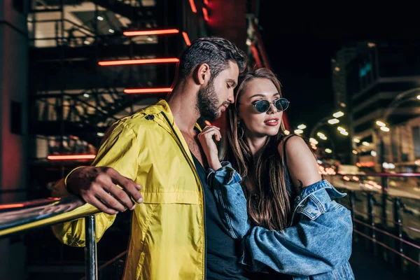 Schöner Freund und attraktive Freundin in Jeansjacke umarmen sich in der Nacht Stadt — Stockfoto