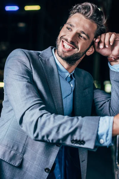 Guapo hombre de negocios en ropa formal sonriendo y mirando hacia otro lado en la ciudad de la noche - foto de stock
