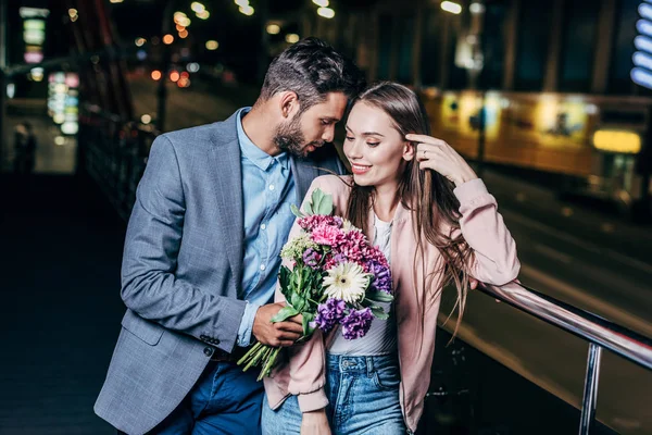 Hombre de negocios guapo dando ramo y besar a mujer atractiva en la ciudad de la noche - foto de stock