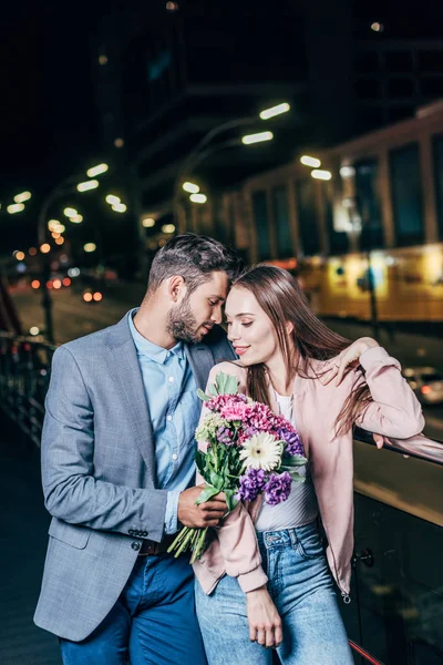Красивый бизнесмен дарит букет и обнимает привлекательную женщину в ночном городе — стоковое фото