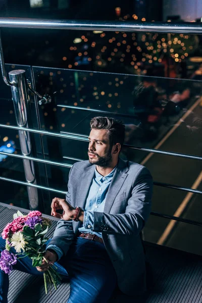 Homem de negócios bonito em desgaste formal com bouquet olhando para longe na cidade noite — Fotografia de Stock