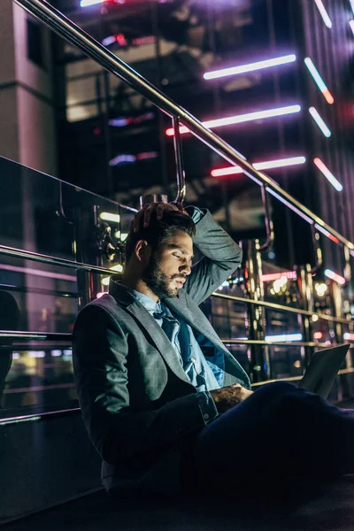 Handsome businessman in formal wear sitting and using laptop in night city — Stock Photo