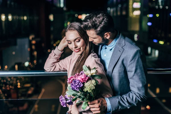 Handsome businessman giving bouquet and hugging attractive woman in night city — Stock Photo