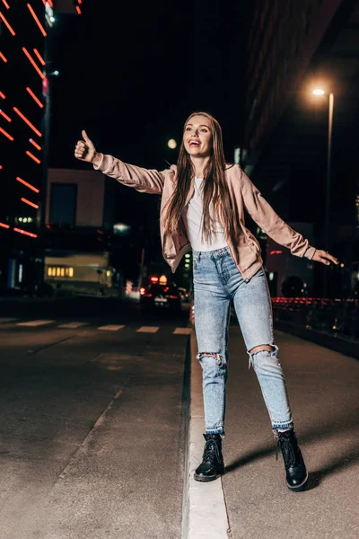 Attrayant femme en rose veste attelage et sourire dans la ville de nuit — Photo de stock