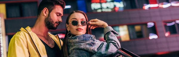 Panoramic shot of handsome boyfriend and attractive girlfriend in denim jacket in night city — Stock Photo