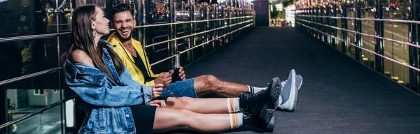 Plano panorámico de novio con botella y novia sonriente sentado en la ciudad de la noche - foto de stock