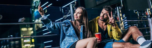 Panoramaaufnahme eines hübschen Freundes mit Friedenszeichen und attraktiver Freundin, der in der Nacht ein Selfie macht — Stockfoto