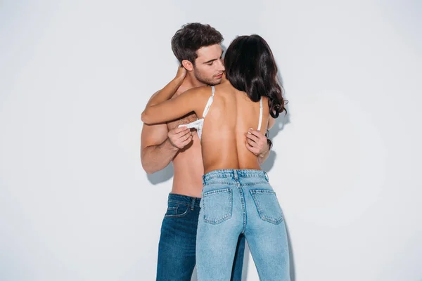 Bonito homem tirando sutiã de menina no azul jeans no cinza fundo — Fotografia de Stock