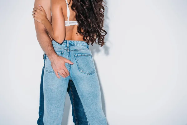 Vista recortada del hombre tocando las nalgas de la chica en vaqueros azules sobre fondo gris — Stock Photo