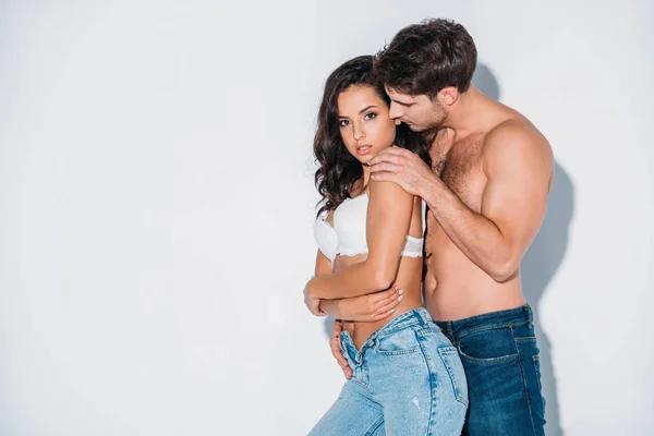 Bonito homem abraçando menina no azul jeans e branco sutiã no cinza fundo — Fotografia de Stock