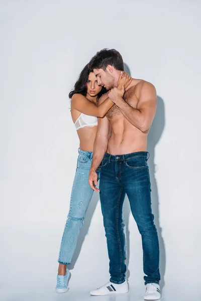 Beautiful girl looking at camera while hugging handsome boyfriend on grey background — Stock Photo