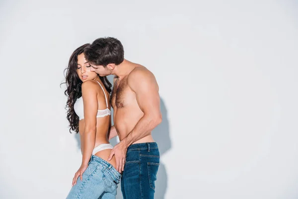 Hombre sin camisa tocando las nalgas y besando novia sobre fondo gris - foto de stock