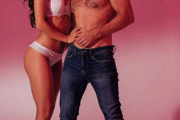 Partial view of sexy girl in white lingerie hugging shirtless man in denim jeans on crimson background — Stock Photo