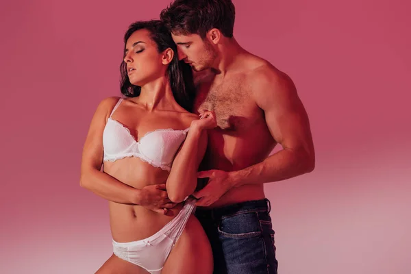Sexy hemdlosen Mann berühren Höschen der verführerischen Mädchen in weißen Dessous auf purpurrotem Hintergrund — Stockfoto
