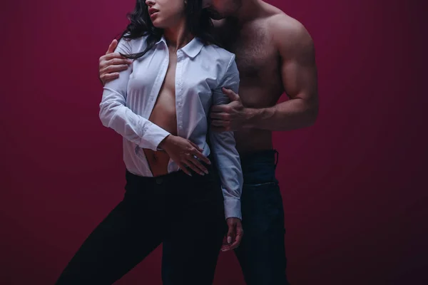 Teilansicht eines hemdlosen Mannes, der sexy Mädchen in ungeknöpftem weißem Hemd auf dunklem Hintergrund umarmt — Stockfoto