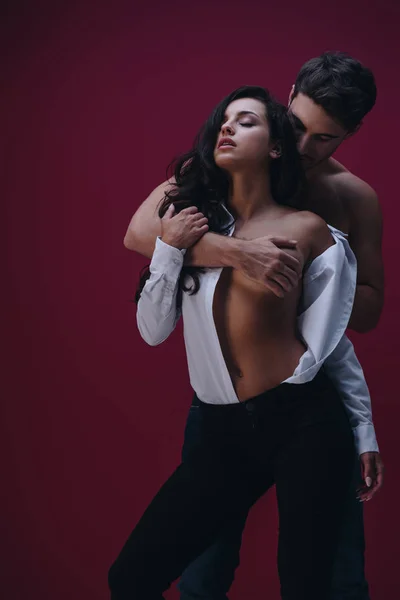 Joven hombre abrazando sexy chica en desabotonado camisa blanca sobre fondo oscuro - foto de stock