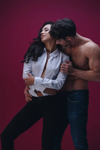 Hombre guapo abrazando a chica atractiva en camisa blanca desabotonada sobre fondo oscuro - foto de stock