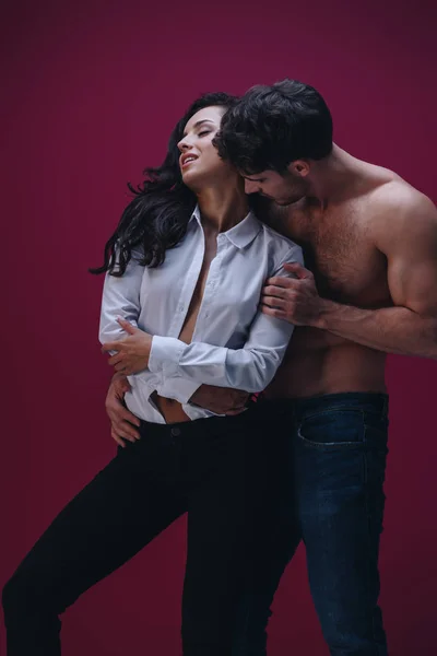 Handsome man embracing attractive girl in unbuttoned white shirt on dark background — Stock Photo