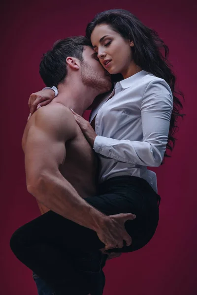 Hombre sin camisa agarrándose de las manos y besándose chica en camisa blanca sobre fondo oscuro — Stock Photo