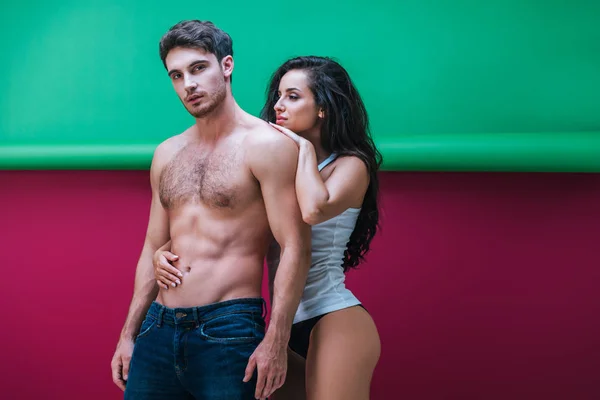 Beautiful girl in sleeveless shirt and panties embracing shirtless man on red and green background — Stock Photo