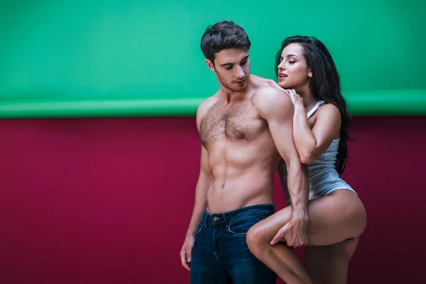 Shirtless man touching leg of sexy girlfriend embracing him on red and green background — Stock Photo