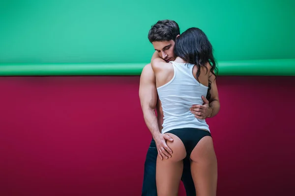 Задний вид сексуальной девушки в рубашке без рукавов и трусиках, обнимающей красивого парня на красном и зеленом фоне — стоковое фото