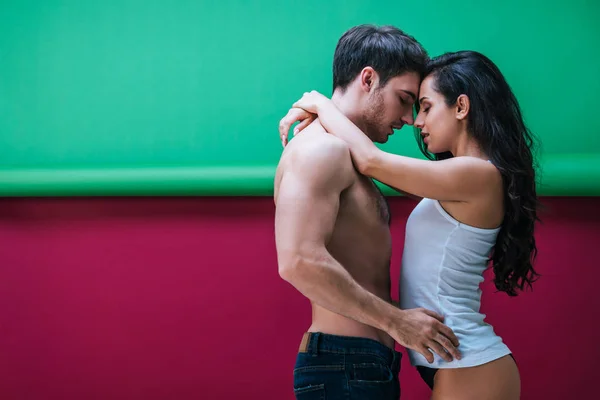 Сексуальная девушка в рубашке без рукавов и трусиках обнимающая бойфренда без рубашки на красном и зеленом фоне — стоковое фото