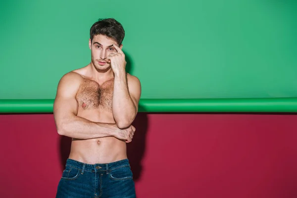 Sexy shirtles homme en jeans denim regardant la caméra sur fond vert et rouge — Photo de stock