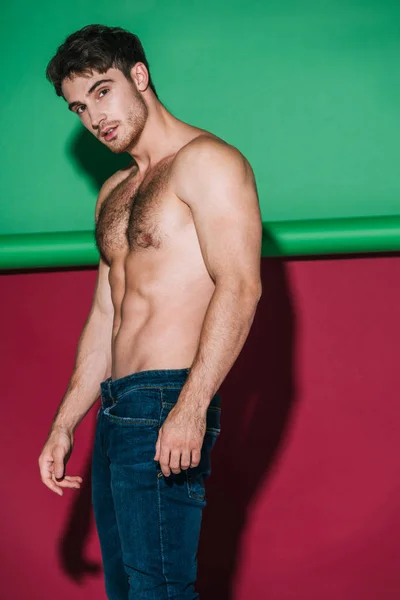 Sexy shirtles homme en jeans denim regardant la caméra sur fond vert et rouge — Photo de stock