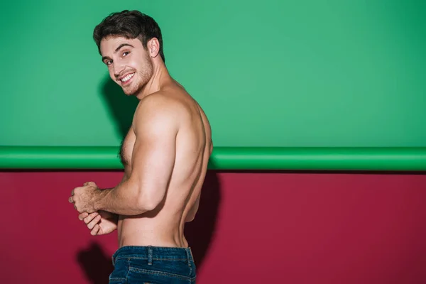 Shirtless, sexy man smiling at camera on green and red background — Stock Photo