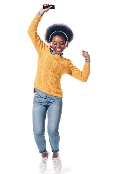 Felice ragazza afroamericana che balla ascoltando musica con le cuffie, isolata su bianco — Foto stock