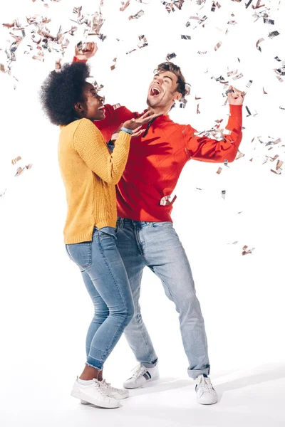 Excitada pareja multiétnica bailando con confeti, aislada en blanco - foto de stock