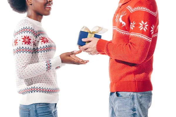 Vista recortada de la pareja multiétnica en suéteres de invierno celebración de la caja de regalo de Navidad, aislado en blanco - foto de stock