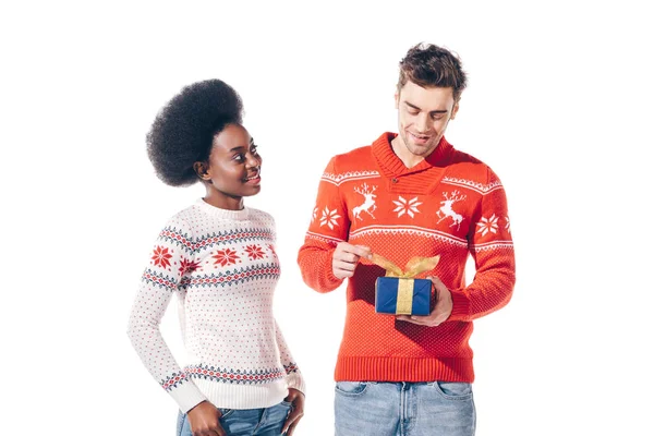 Multiethnic couple in winter sweaters holding christmas present, isolated on white — Stock Photo