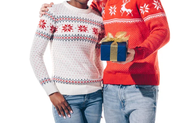 Vista recortada de pareja interracial en suéteres de invierno celebración de Navidad presente, aislado en blanco - foto de stock