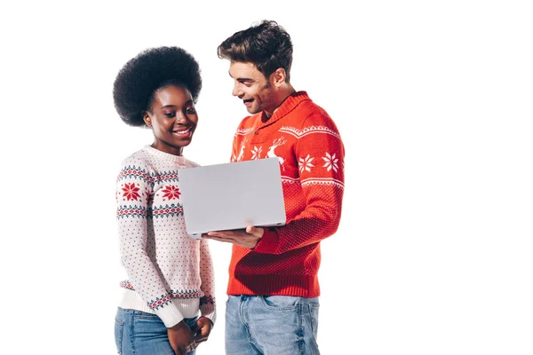 Sourire couple multiculturel en chandails à l'aide d'un ordinateur portable, isolé sur blanc — Photo de stock