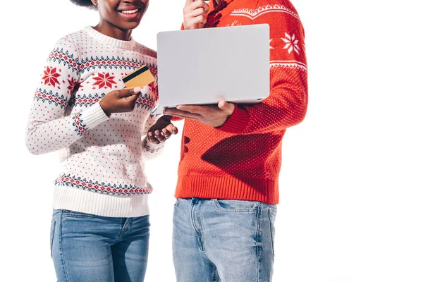 Vista cortada de casal interracial segurando usando laptop com cartão de crédito, isolado no branco — Fotografia de Stock